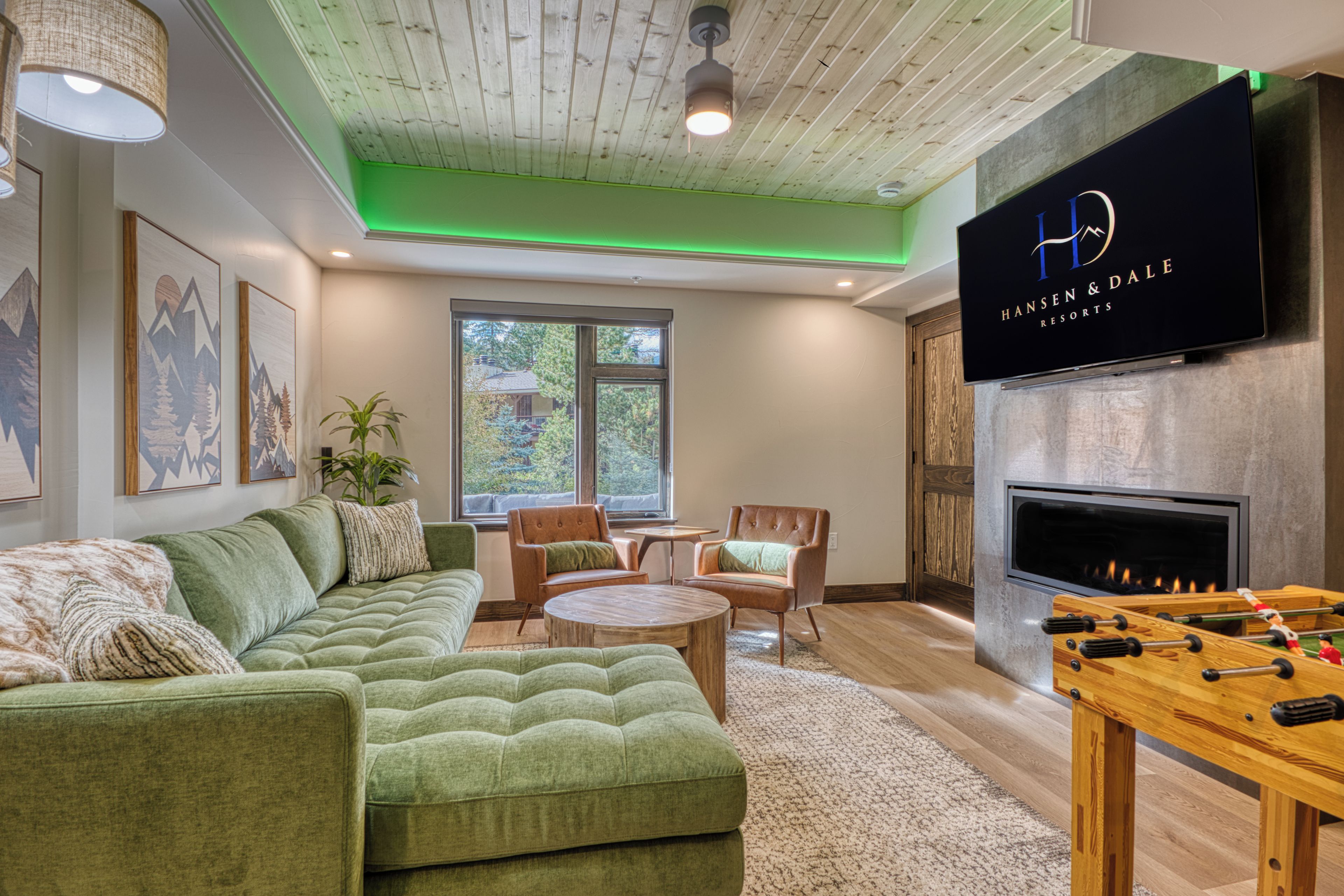 A modern living room with a green sectional sofa, a fireplace, and a television displaying 'Hansen & Dale Resorts'.