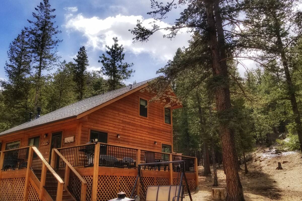 Une cabane en bois dotée d’un balcon, entourée de grands arbres et surplombant un ciel dégagé.