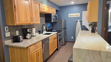 A modern kitchen with wooden cabinets, a stainless steel refrigerator, a built-in oven, and a coffee maker.