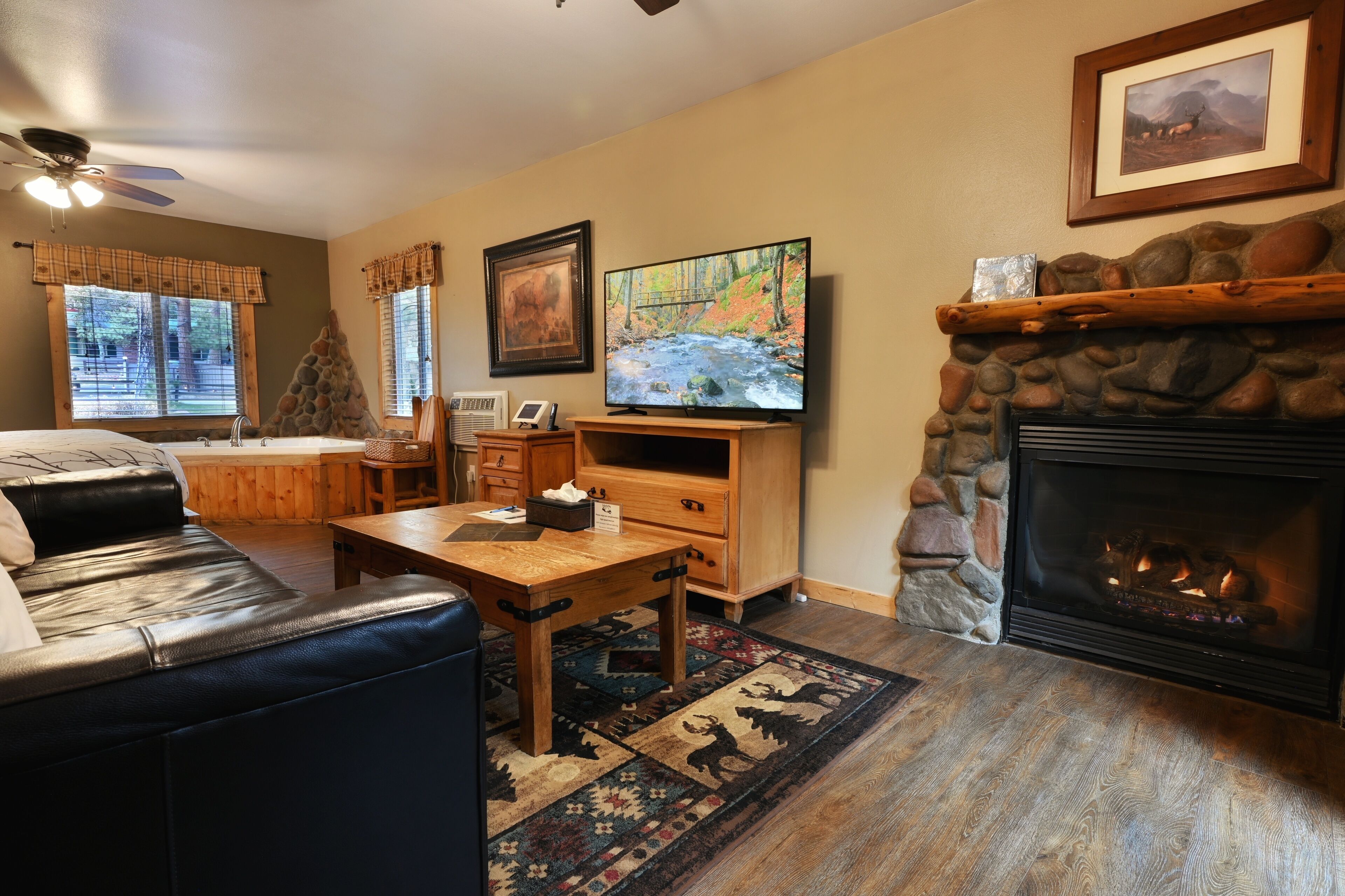 A living room with a fireplace, a television, a stone wall, and a window with a view of trees.
