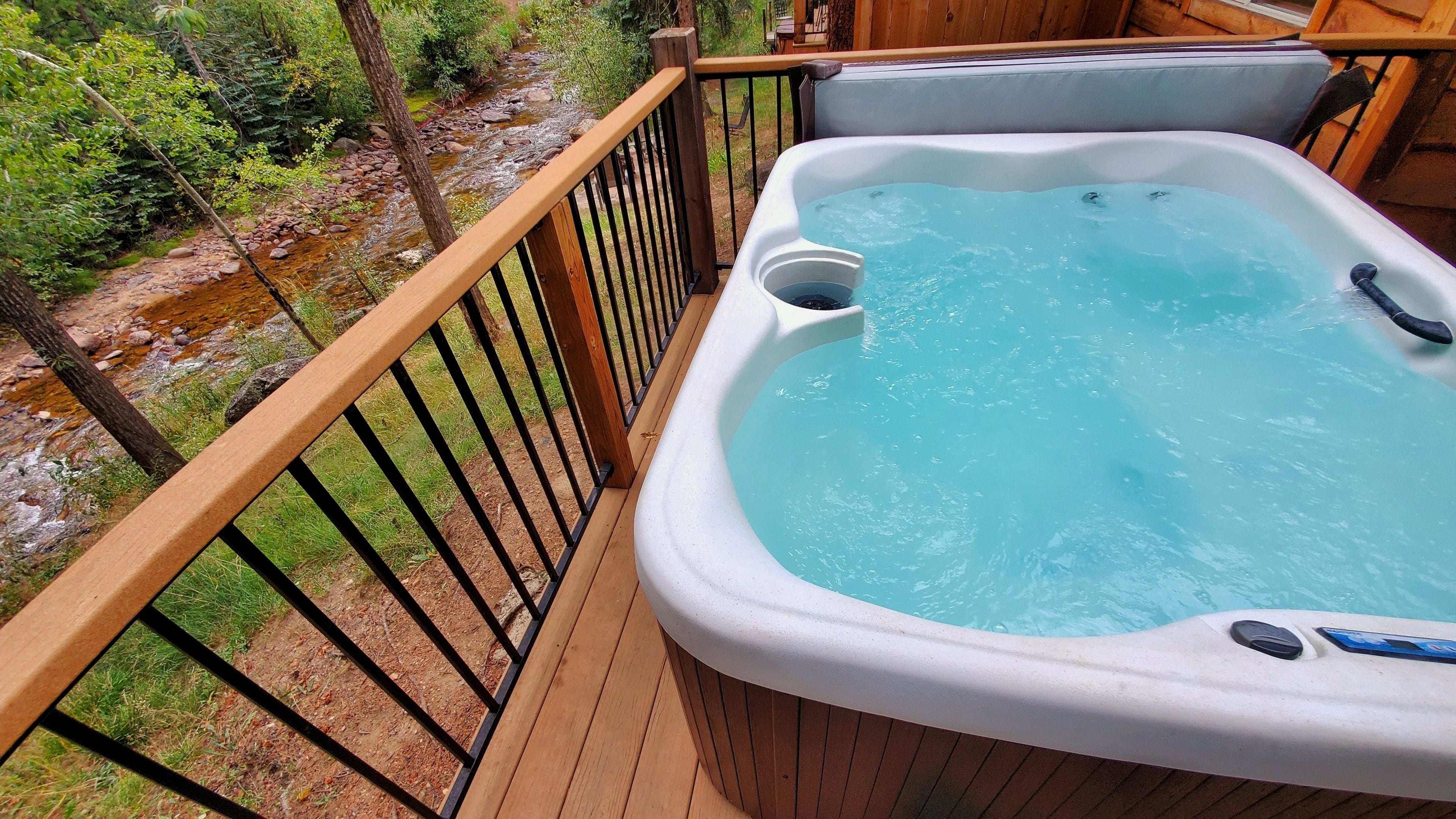 Un bain à remous sur une terrasse en bois, avec vue sur un ruisseau aux rochers.