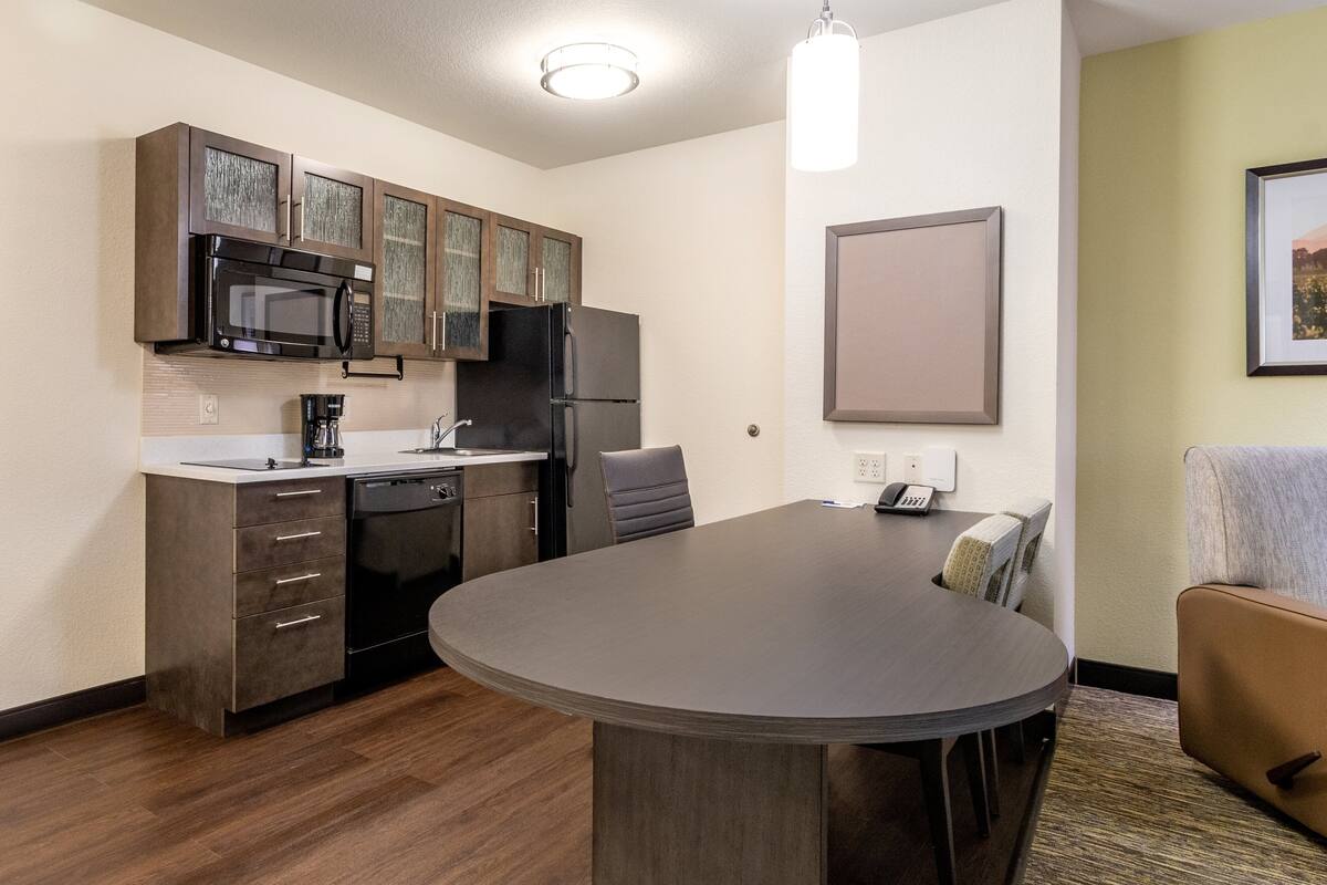 Una cocina compacta equipada con microondas, refrigerador y lavavajillas. Hay una mesa de comedor con sillas y un pequeño sofá.