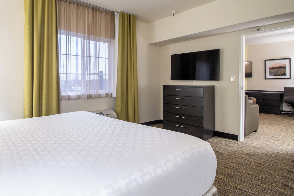 Quarto de hotel com uma cama grande, televisão de tela plana na parede, cômoda escura e escrivaninha com cadeira.
