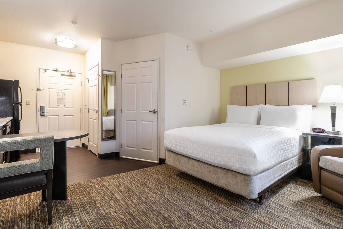 Una habitación de hotel con cama, escritorio, silla, lámpara y puerta.