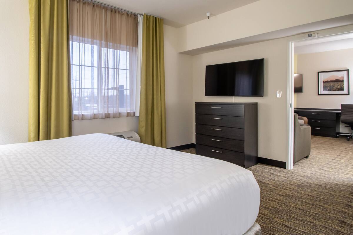 Habitación de hotel con una cama grande, un televisor de pantalla plana en la pared, un aparador de color oscuro y un escritorio con una silla.