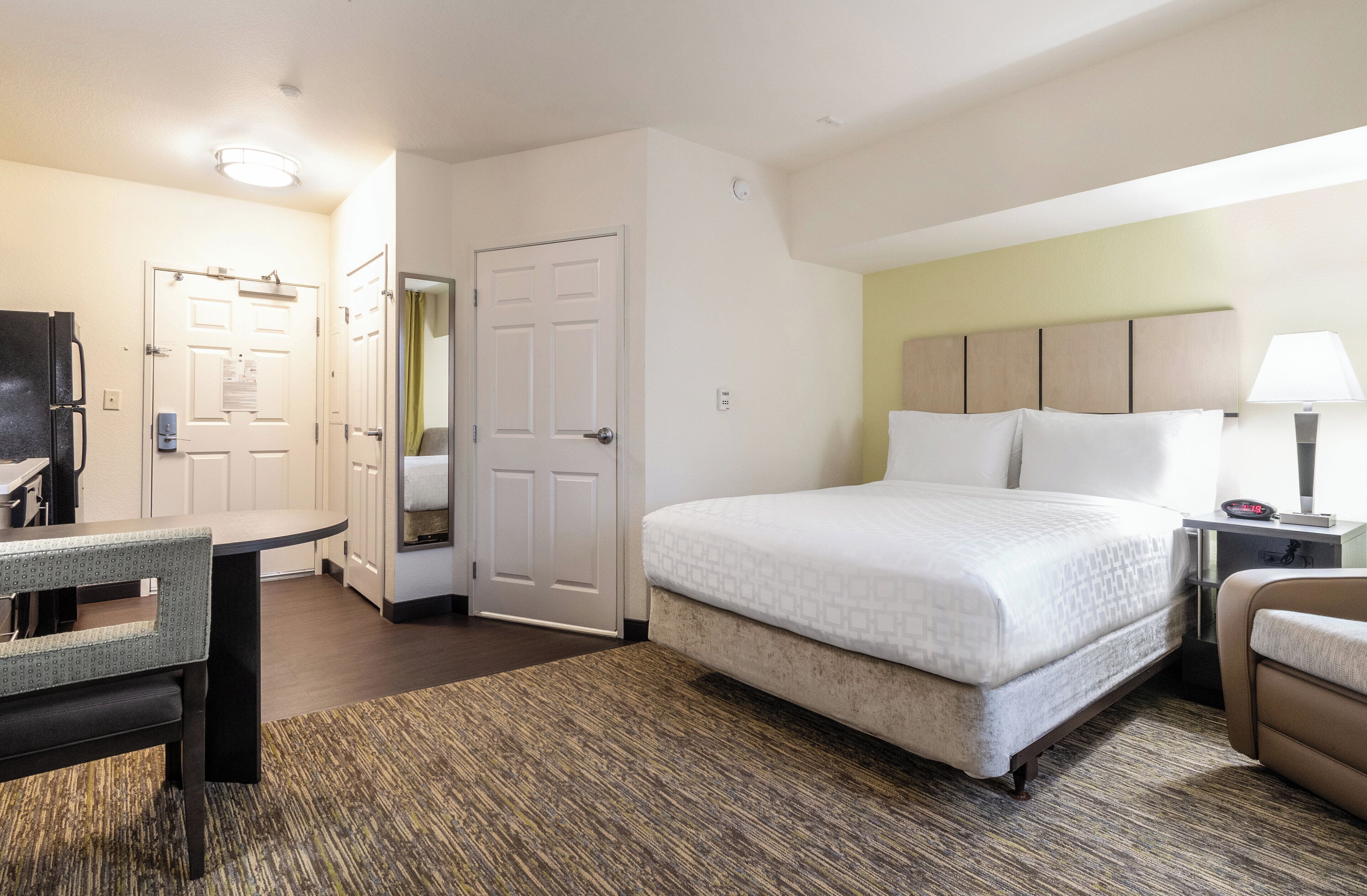 Habitación de hotel con cama, escritorio, silla, lámpara y puerta.