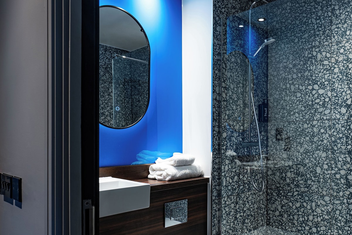A modern bathroom with a marble shower, a round mirror, and a white sink.