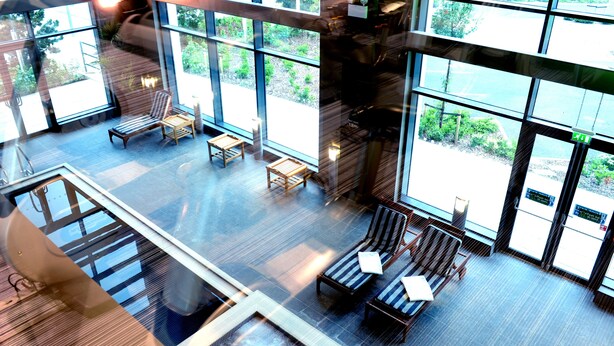 A spacious indoor area with large windows, wooden flooring, and several seating areas. - Village Hotel Farnborough (Farnborough)