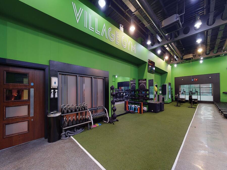 A gym with green walls, weightlifting equipment, treadmills, and a sign reading "VILLAGE GYM".