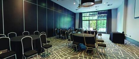 Un salón de conferencias con alfombra estampada, mesas redondas y sillas.