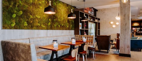 A restaurant with a green moss wall, wooden tables, cushioned seating, and pendant lighting.