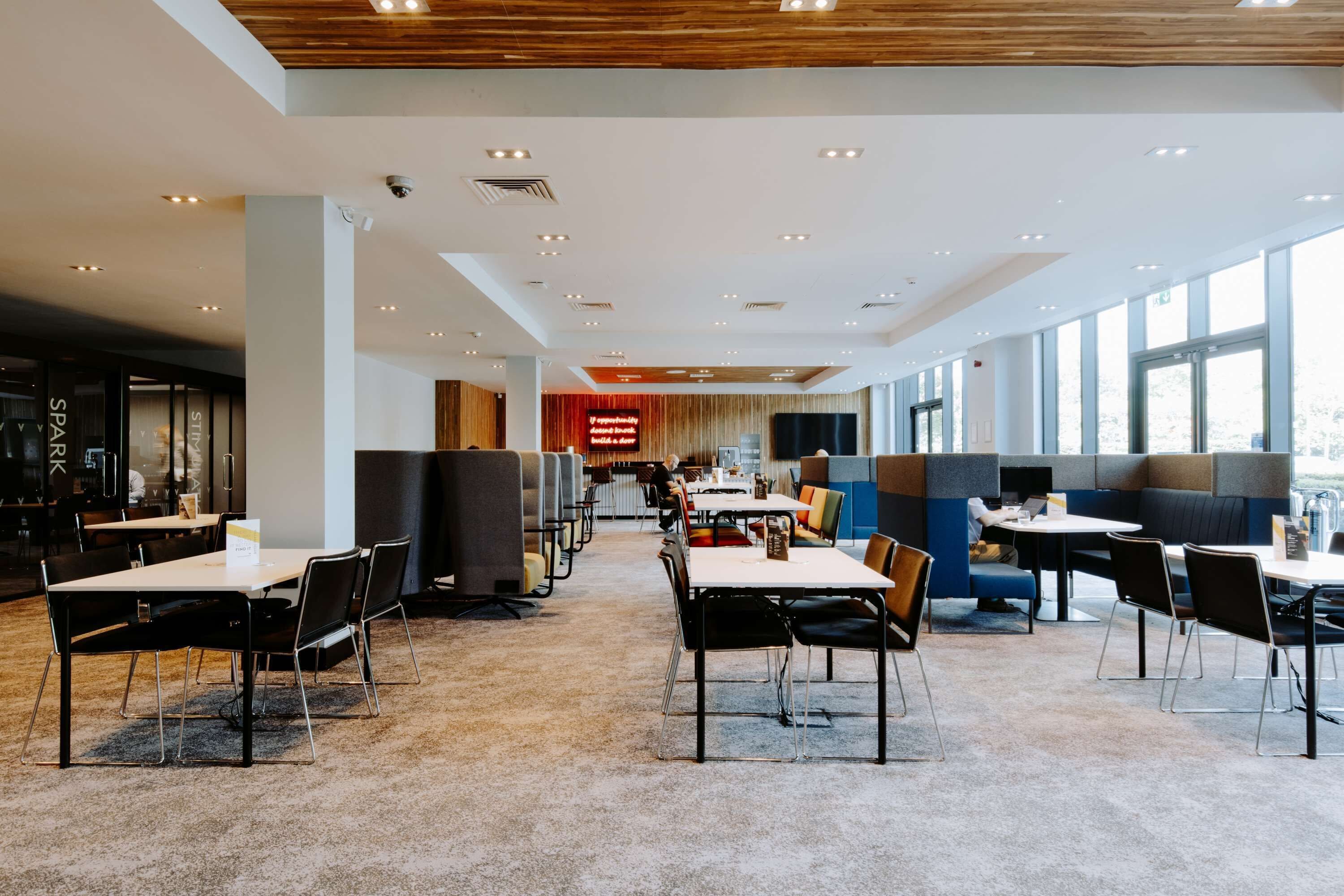 A modern dining area with booths and tables, large windows, and a high ceiling with recessed lighting.