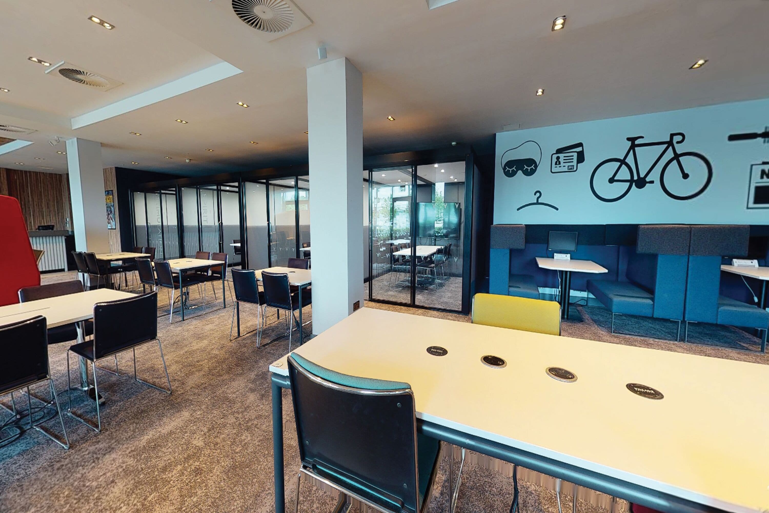 Un espace de bureau moderne, doté de tables et de chaises, d’une décoration murale sur le thème du vélo et offrant une vue sur l’extérieur.