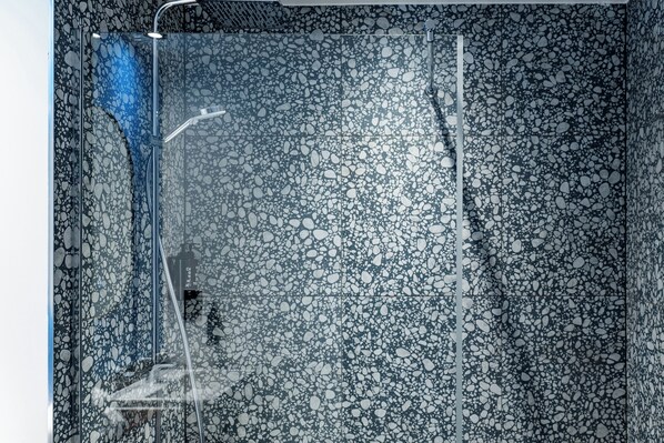 A modern shower enclosure with a pebble-textured wall and a glass door. - Village Hotel Farnborough (Farnborough)