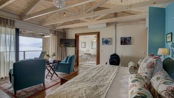 A cozy room with a large bed, a sofa, a chair, and a view of the sea.