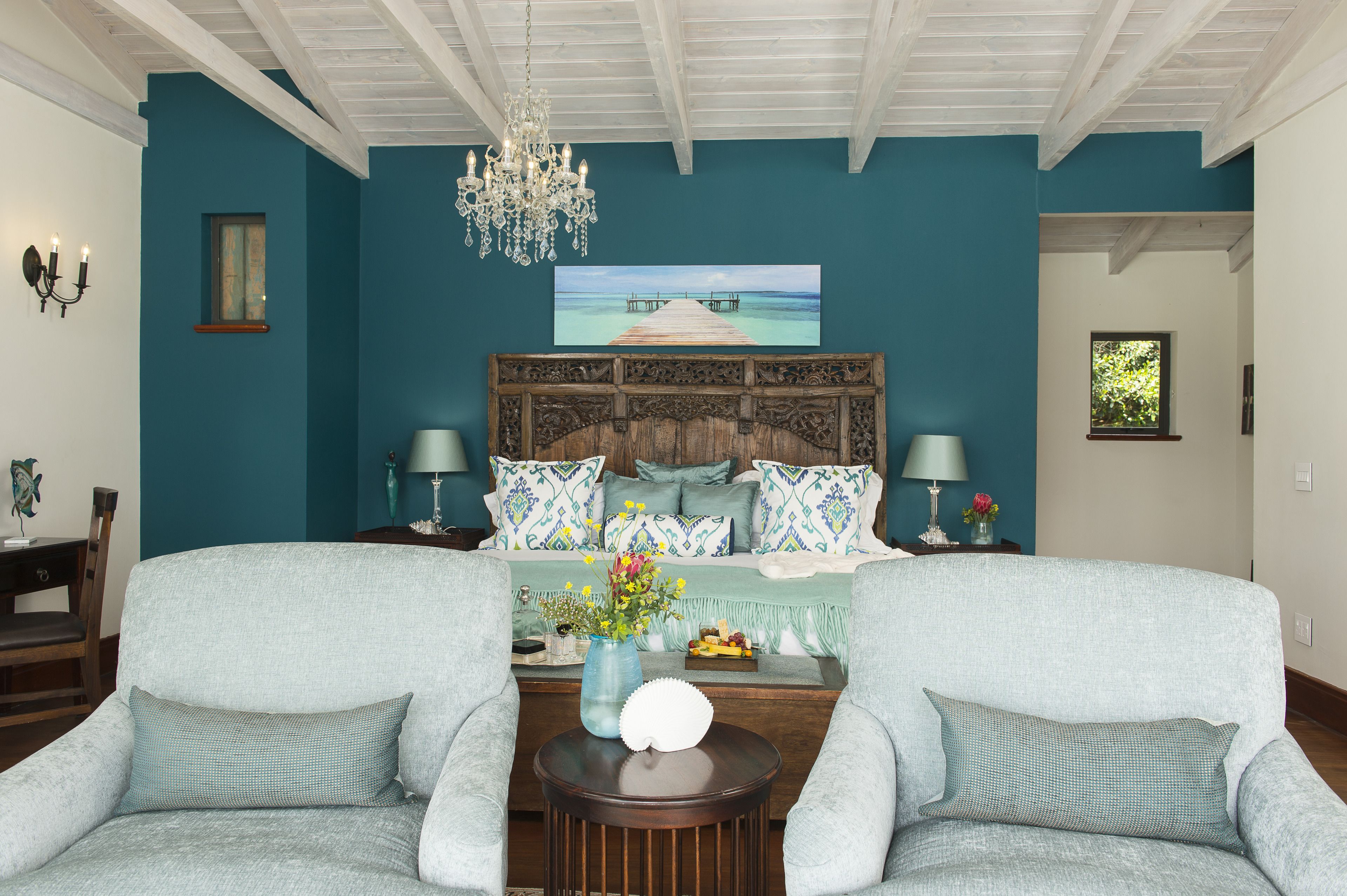 A bedroom with teal walls, a wooden headboard, a chandelier, and a large window.