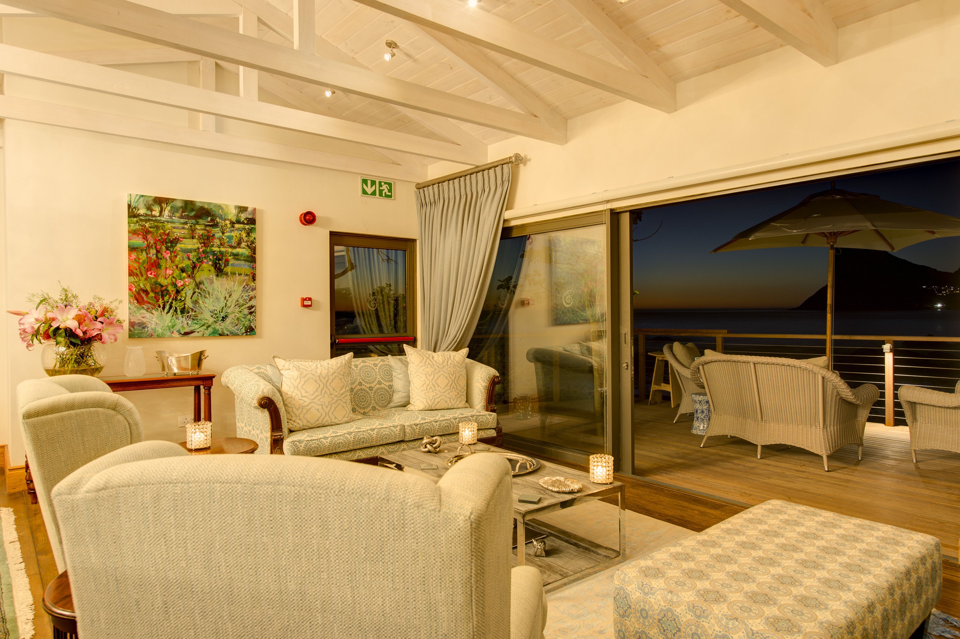 Un rincón tranquilo con sofá, sillones y una mesa de comedor. Un cuadro grande decora la pared, y una puerta de cristal da a un balcón exterior.