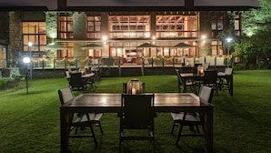 A well-lit outdoor dining area with multiple tables and chairs, surrounded by a stone wall and a grassy lawn. - Riboville (Midrand)