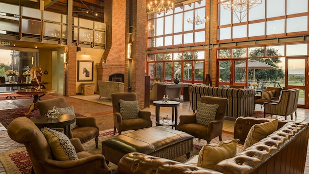 A spacious lobby with high ceilings, large windows, and a fireplace. There are multiple seating areas with leather sofas and armchairs. - Riboville (Midrand)