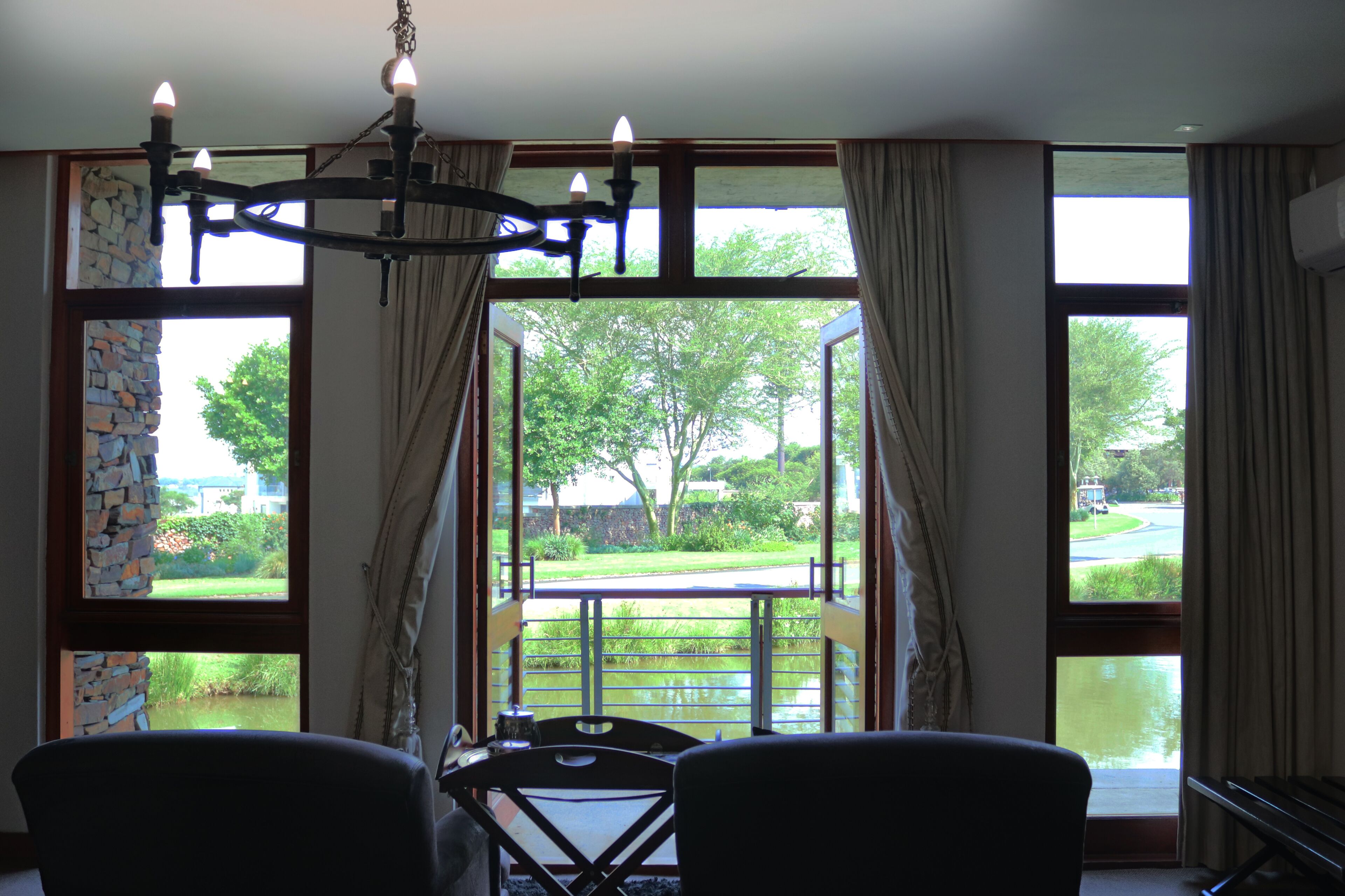 A room with a dining table and chairs, large windows with curtains, a stone wall, and a chandelier.
