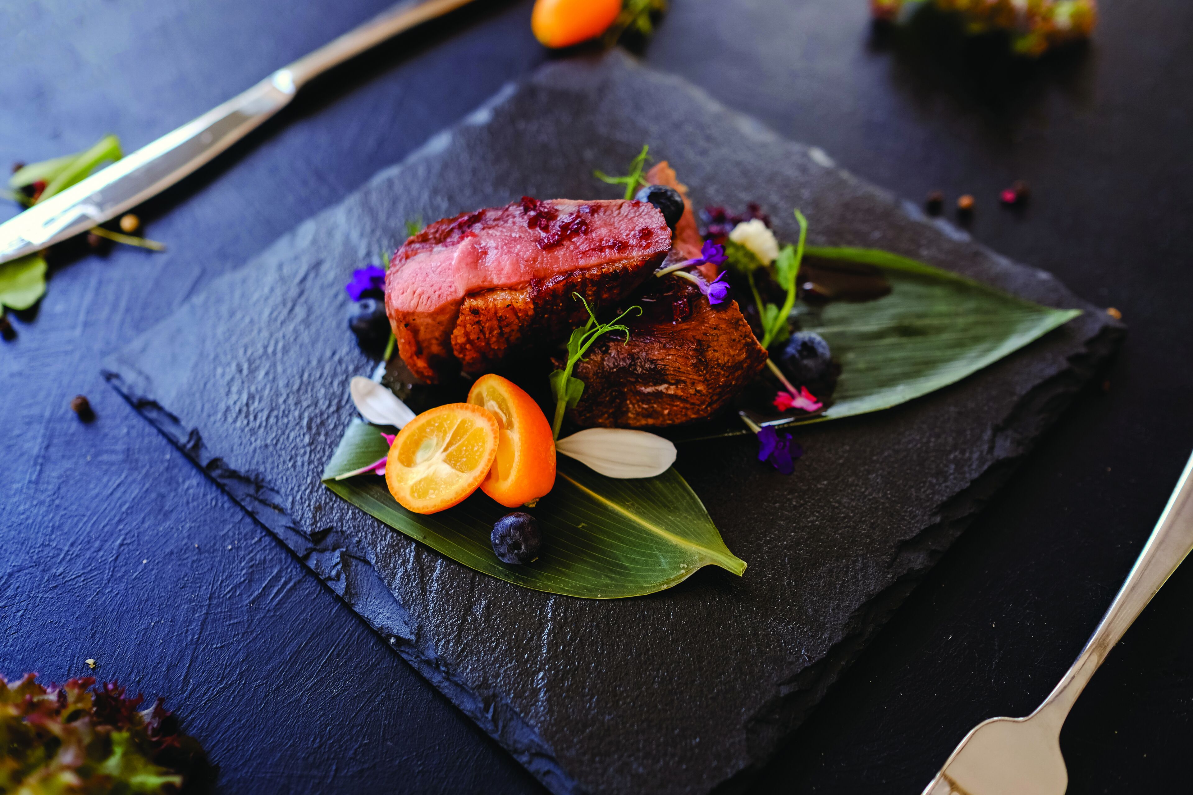 A steak with fruit and flowers on a slate plate.
