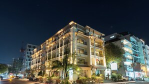 Un hotel de varios pisos con balcones, una entrada bien iluminada y un área ajardinada con plantas.