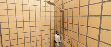 A bathroom with a tiled wall, a showerhead, and a shelf with toiletries.
