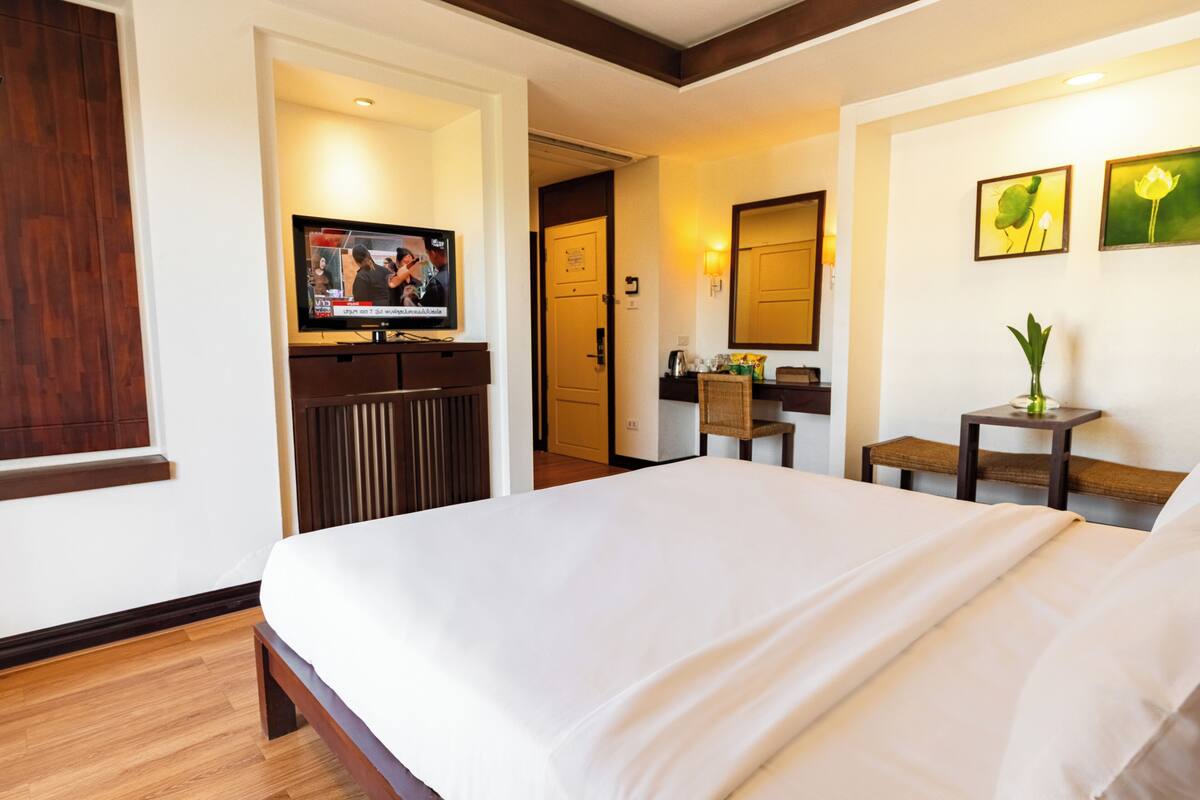 A hotel room with a bed, a television, a desk with a chair, and a small table with a vase.