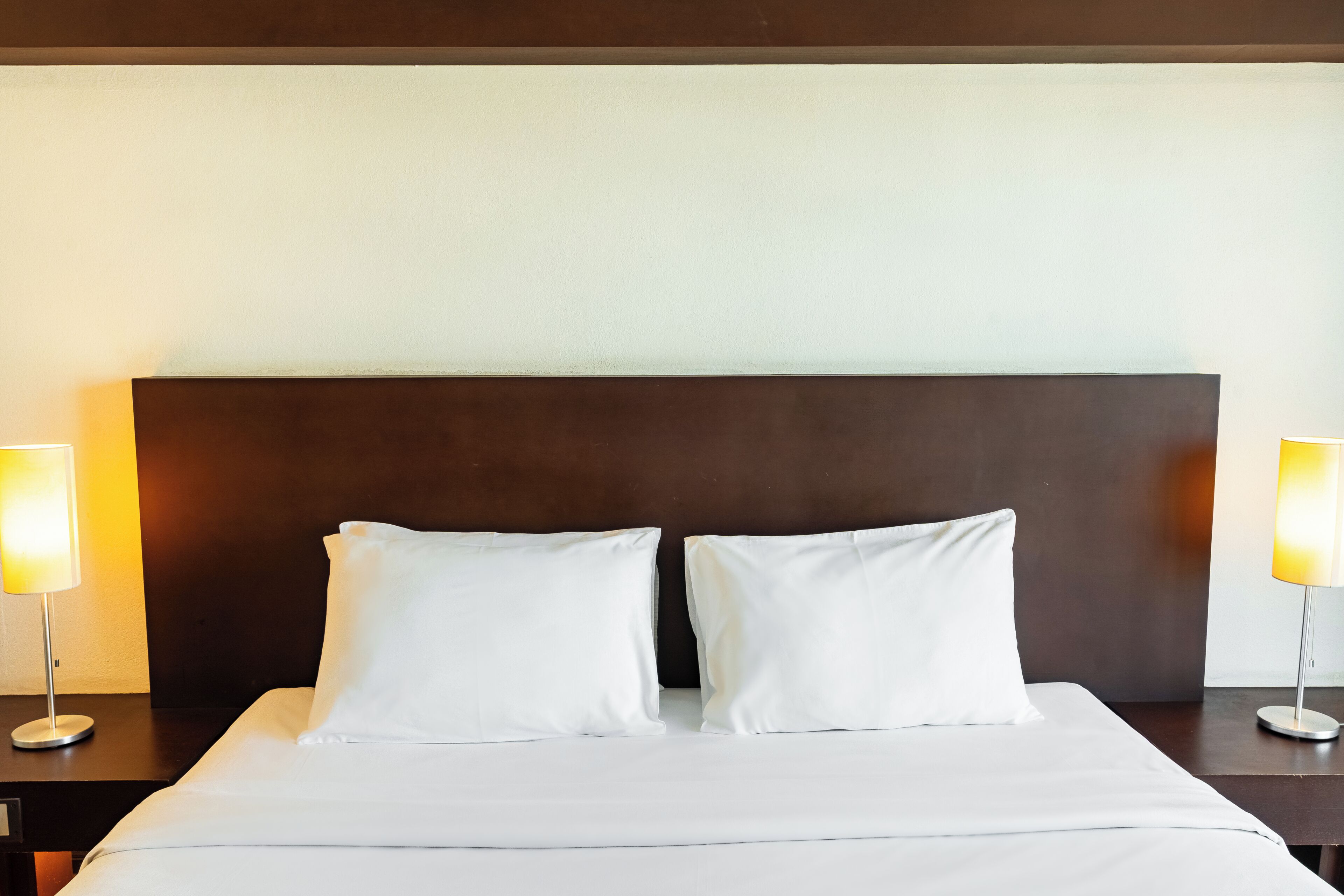 A neatly made bed with white linens, two bedside lamps, and a dark headboard.