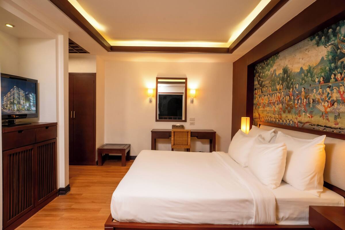 A hotel room with a bed, a desk, a television, and a large painting on the wall.