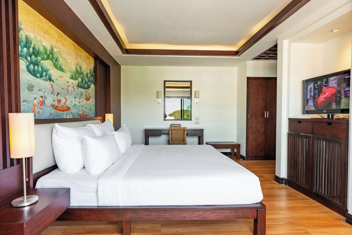 A hotel room with a large bed, a desk, a television, and a mural on the wall.