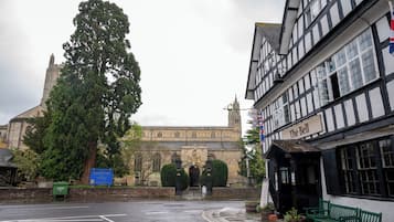 A historic building with a large tree in front, a pub named "The Bell" to the right, and a sign indicating a church nearby.