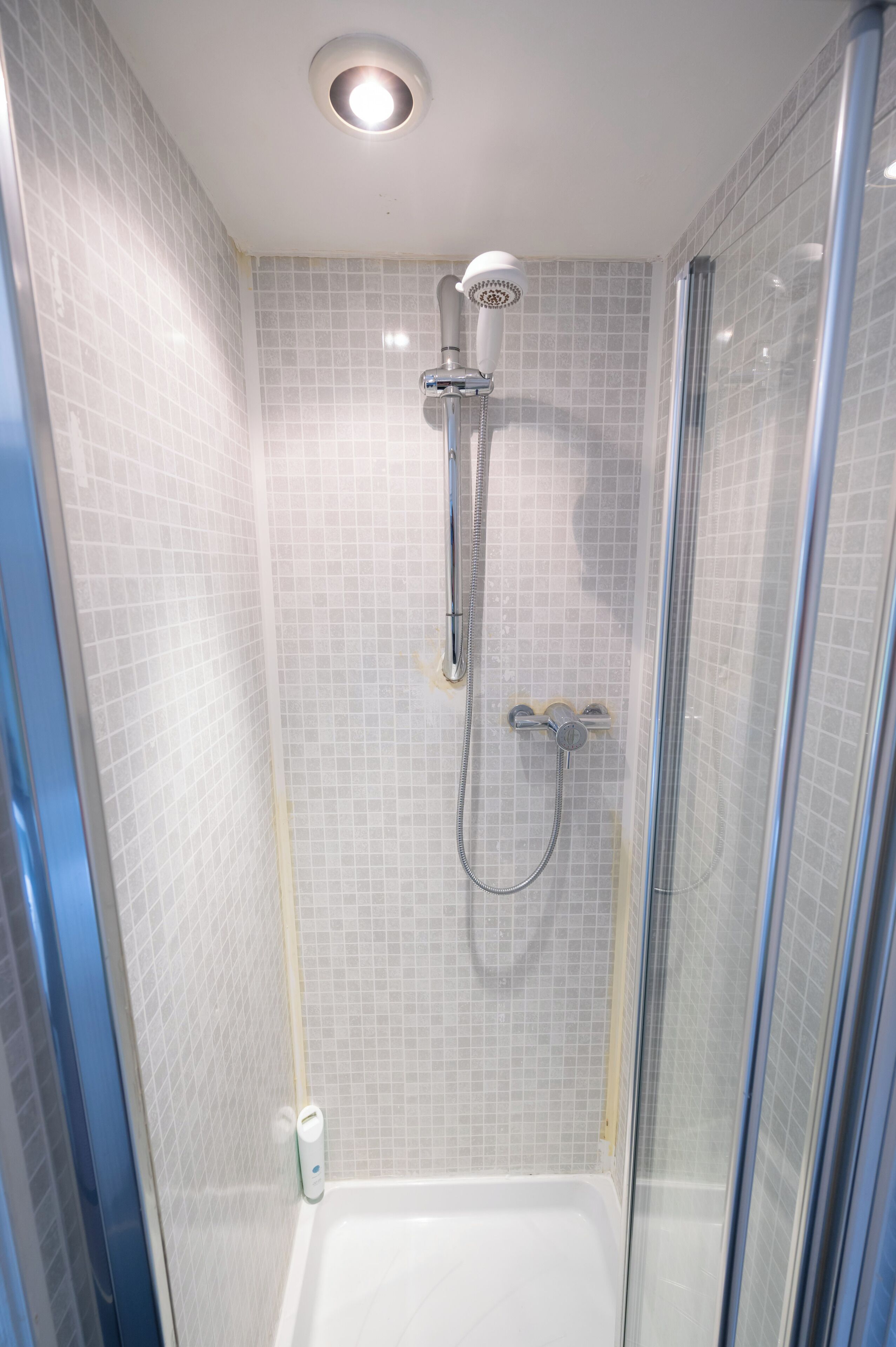 A shower with a glass door, a handheld showerhead, and a wall-mounted faucet.