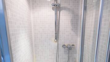 A shower with a glass door, a handheld showerhead, and a wall-mounted faucet.