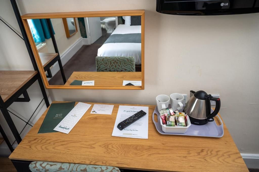 Een hotelkamer met een houten bureau, een dienblad met waterkoker, kopjes en een afstandsbediening.