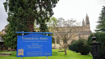 Un cartel de la Abadía de Tewkesbury, una iglesia histórica con un árbol grande y un farol al frente.