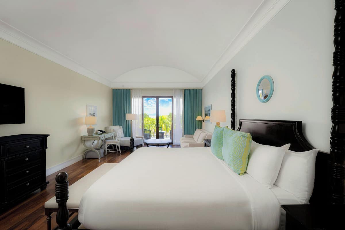 A hotel room with a large bed, a desk, a chair, a small table, and a TV.