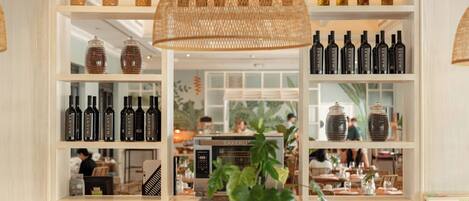 A restaurant interior with shelves of wine bottles, a central table with a plant, and a visible kitchen area.