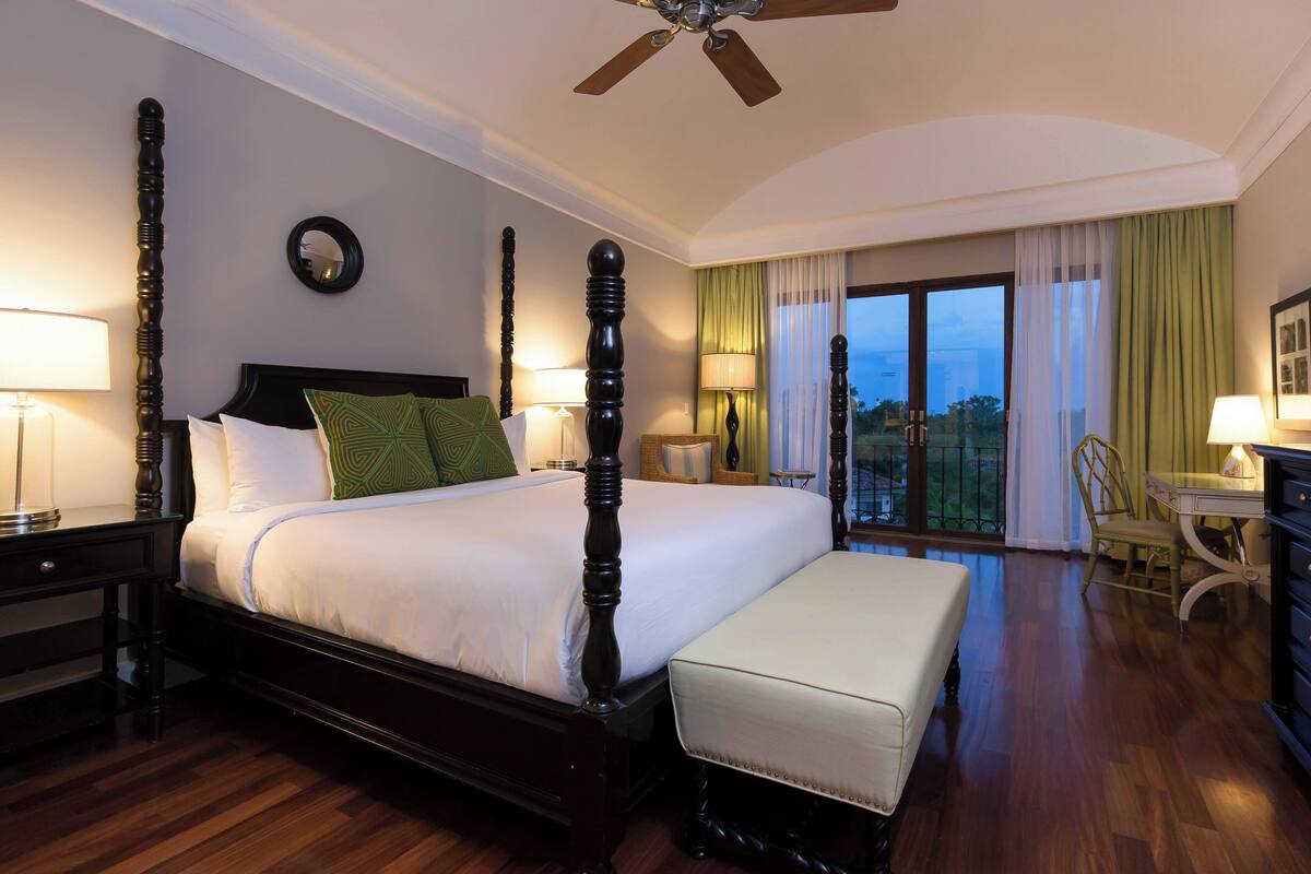 A hotel room with a large bed, a desk, a chair, and a balcony with a view.