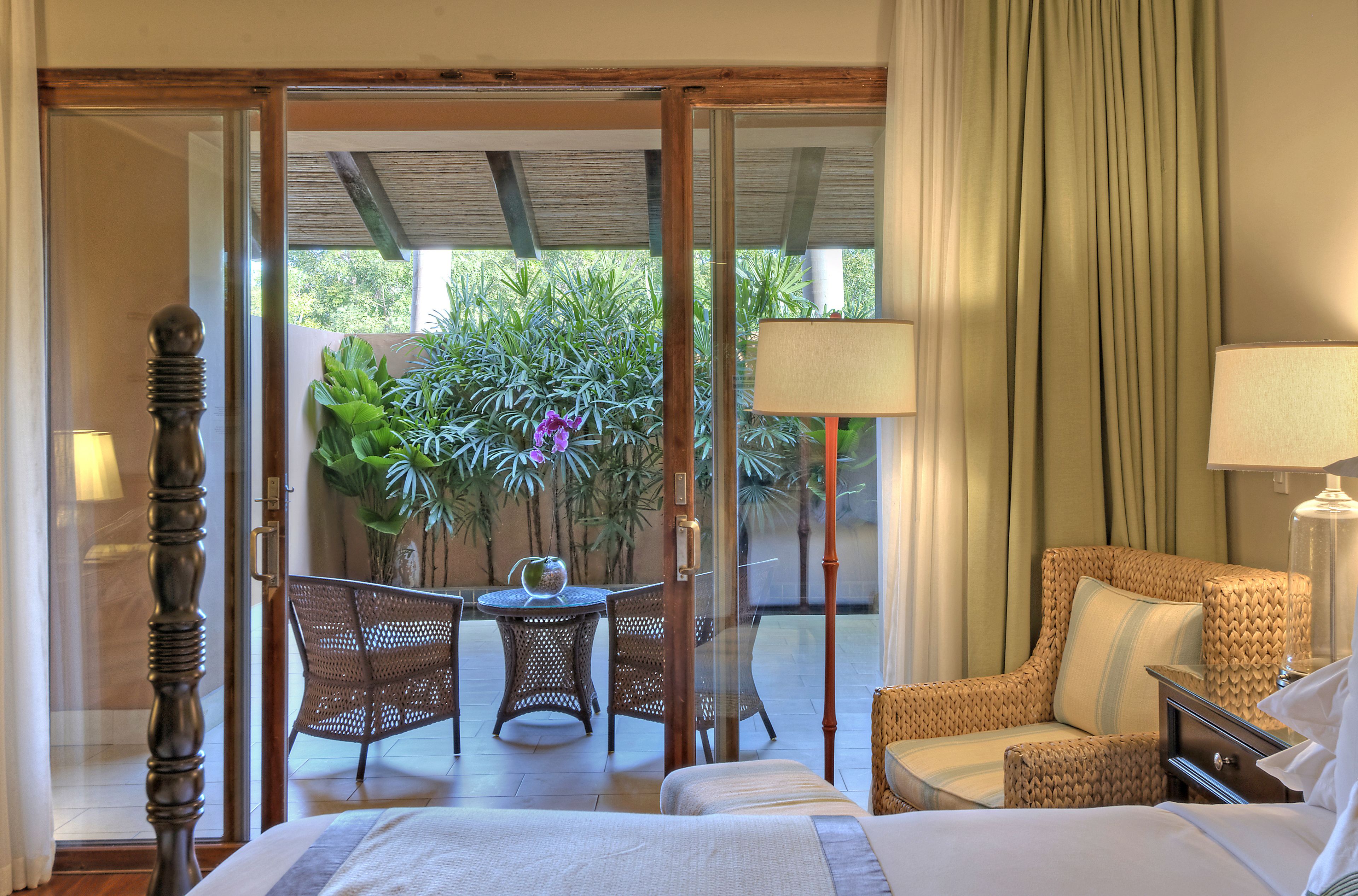 Habitación de hotel con cama, zona de estar con mesa y sillas, y vista al jardín por una puerta de cristal.