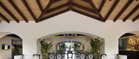A spacious lobby with a high wooden ceiling, arched doorways, and a central seating area with chairs and tables.