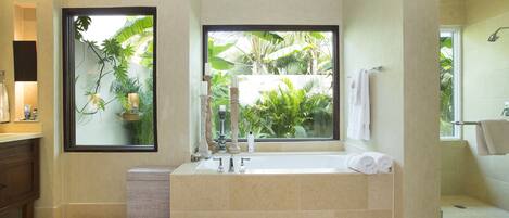 Une salle de bain moderne dotée d’une grande baignoire, d’une douche et d’une fenêtre offrant une vue sur la végétation tropicale.