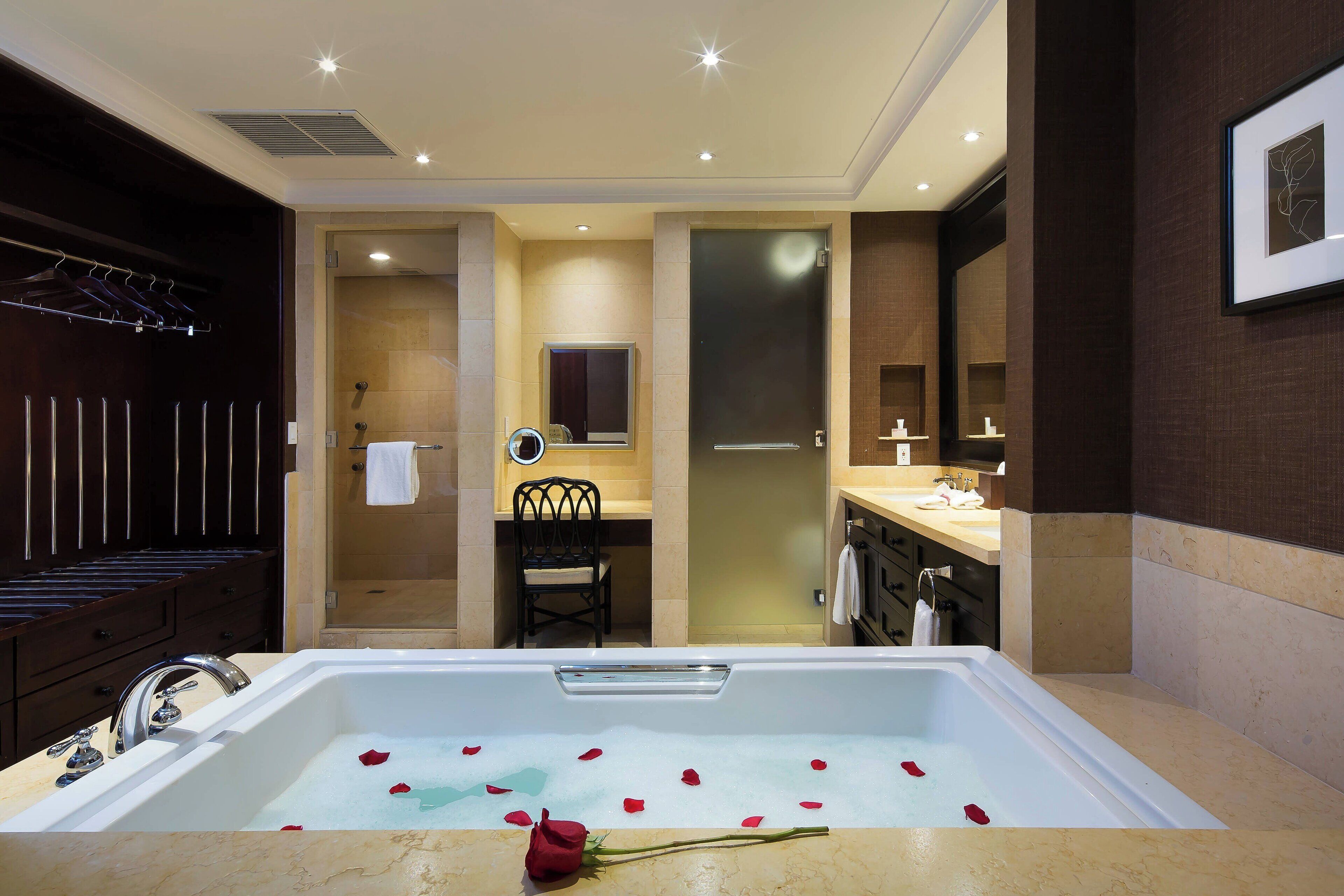 A bathroom with a bathtub filled with rose petals, a mirror, a chair, and a vanity with a towel rack.