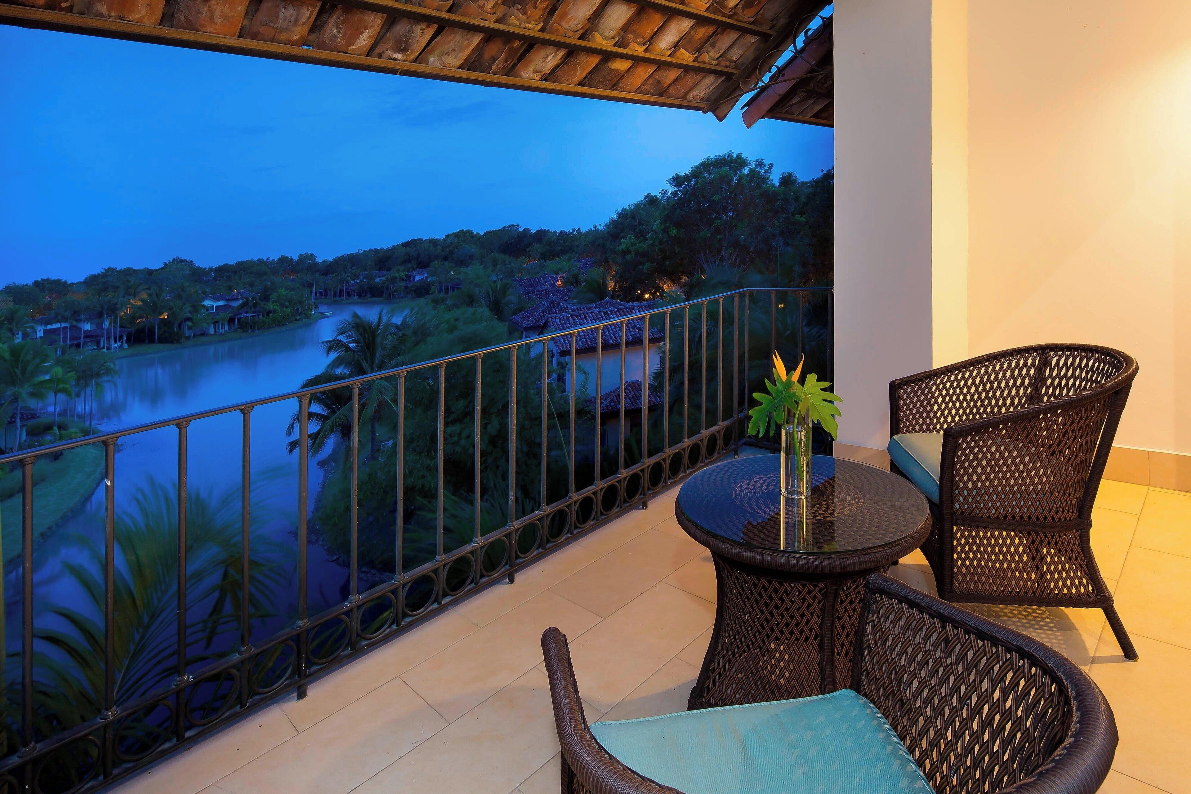 Een balkon met rieten meubels, uitzicht op een rivier en een rieten dak.