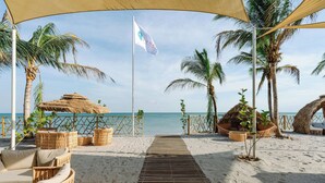 A beach with a wooden pathway leading to a thatched-roof structure, surrounded by palm trees and wicker furniture. - The Buenaventura Golf & Beach Resort Panama, Autograph Collection (El Chiru)