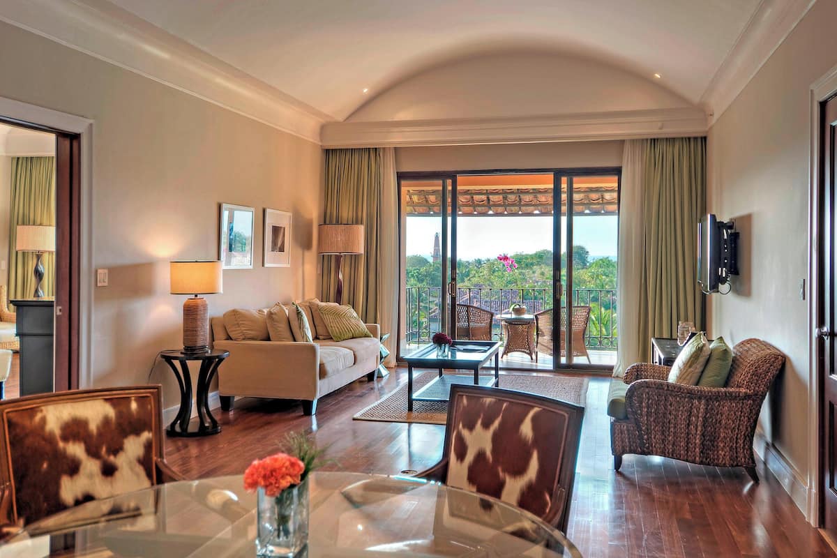 A spacious living area with a sofa, armchairs, a coffee table, and a dining table with a vase of flowers.