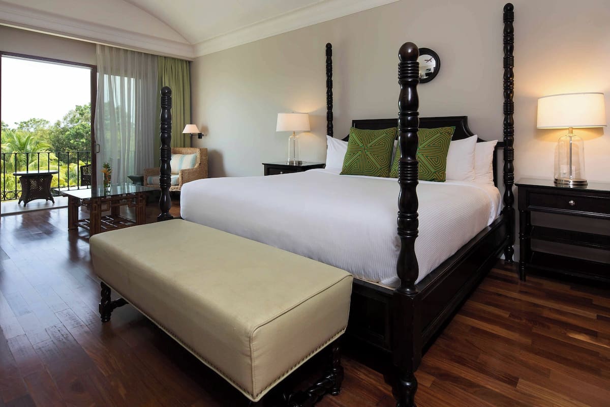 A spacious bedroom with a four-poster bed, a bench, and a balcony with a table and chairs.