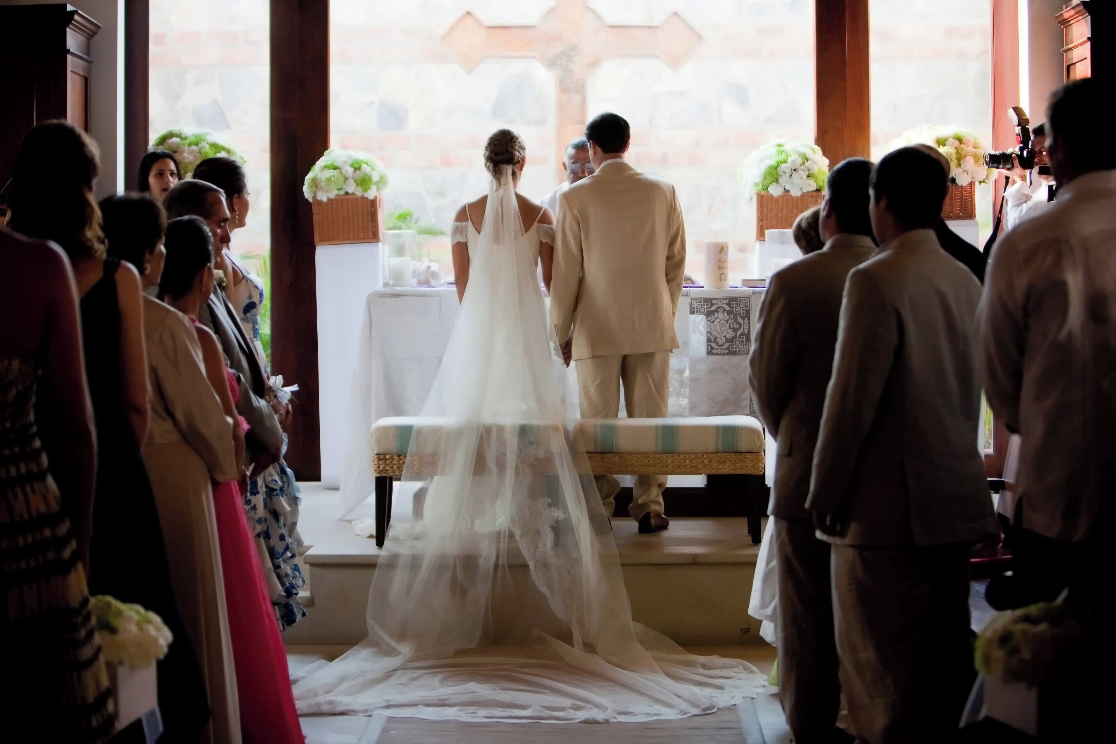 A wedding ceremony with a bride and groom facing the altar, surrounded by guests.
