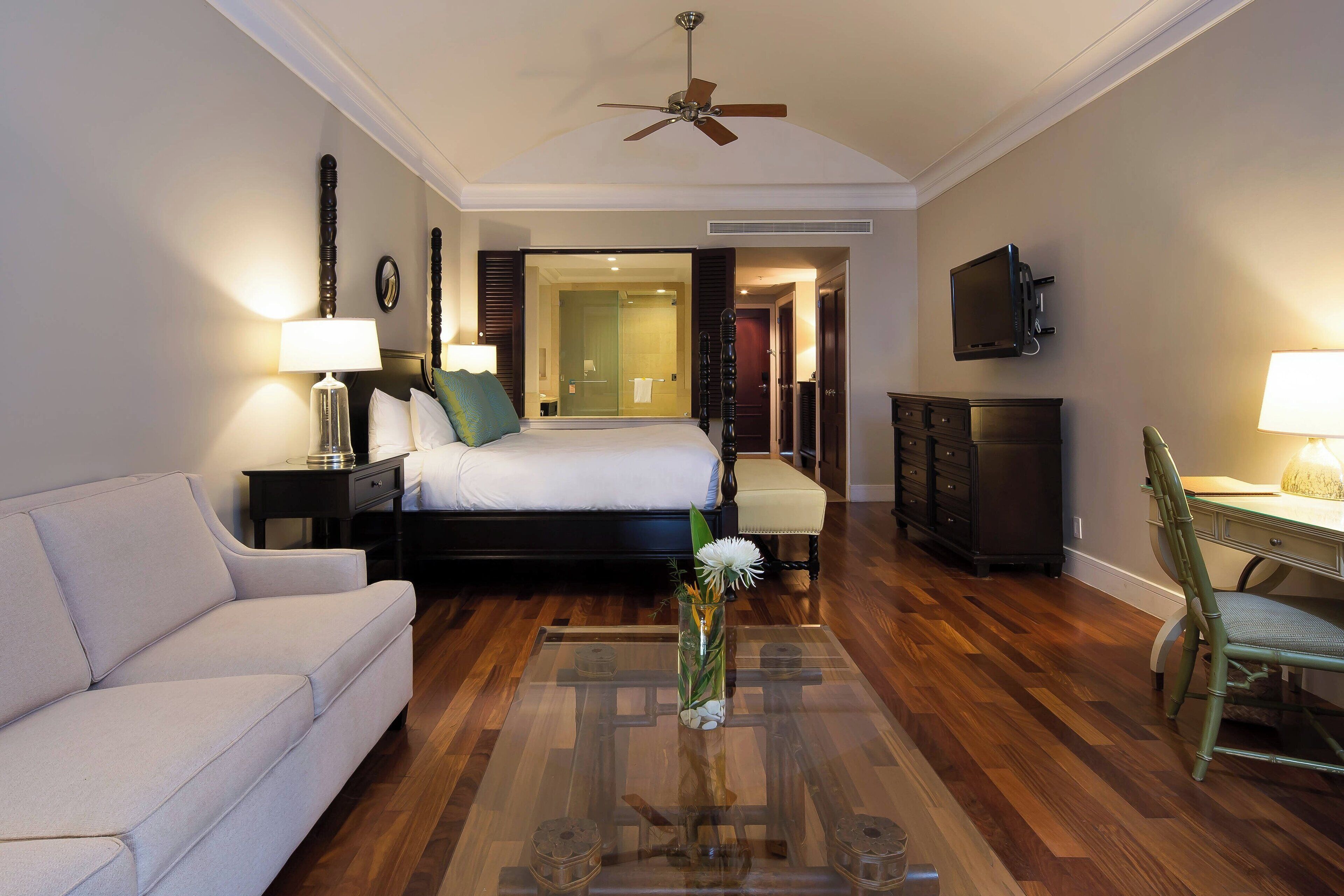 Una habitación de hotel con cama, sofá, escritorio, televisor y ventilador de techo.