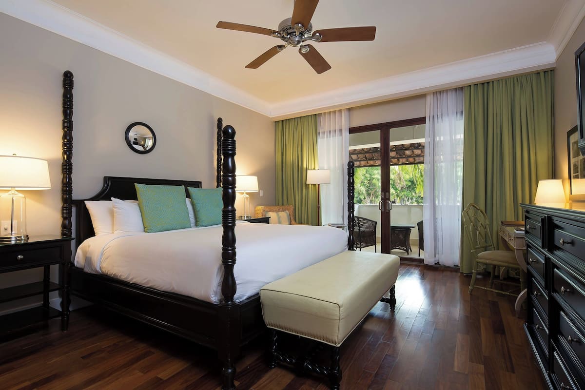 A four-poster bed with a wooden headboard, a bench at the foot of the bed, and a ceiling fan.